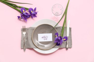 Tebrik kartı ve pembe arka planda süsen çiçekleri olan güzel bir masa. Anneler Günü kutlaması