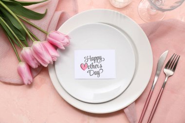 Tebrik kartı ve pembe arka planda lale çiçekleri olan güzel bir masa. Anneler Günü kutlaması