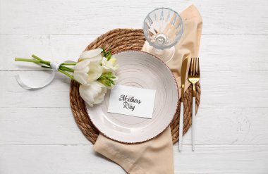 Tebrik kartı ve beyaz ahşap arka planda güzel çiçekler olan şık bir masa. Anneler Günü kutlaması