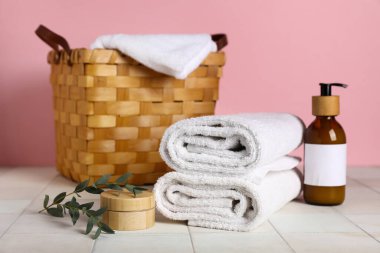 Temiz havlular, kozmetik ürünler ve açık fayanslı sepet pembe arka planda.