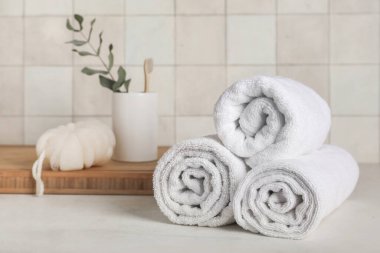 Yuvarlak temiz havlular, banyo süngeri, diş fırçası ve okaliptüs dalı açık fayans duvara karşı masada.