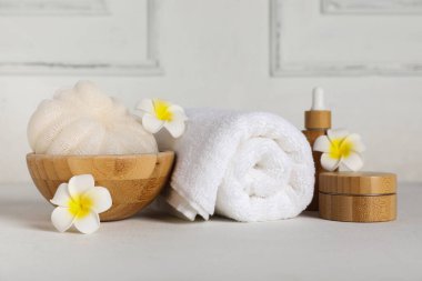 Temiz havlu, banyo süngeri, kozmetik ürünleri ve ışık masasında tropikal çiçeklerle kompozisyon