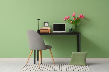 Modern dizüstü bilgisayarı, kitapları ve yeşil duvarın yanındaki güzel lale çiçekleriyle süslü çalışma alanı.