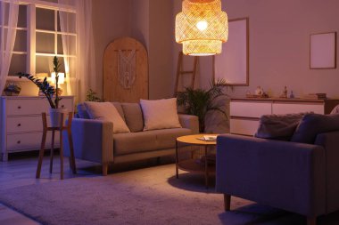 Geceleri kanepeleri, masası ve parlayan lambası olan oturma odasının içinde.