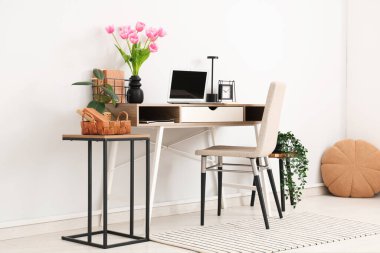 Tabureler, ev bitkileri, dizüstü bilgisayarlar ve vazoda güzel lale çiçekleri olan modern işyerinin içini.