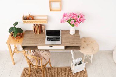 Tabureleri, rafları, dizüstü bilgisayarı ve vazosunda güzel lale çiçekleri olan modern işyerinin içini.