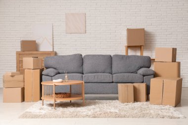 Oturma odasının içinde kanepe, sehpa ve beyaz tuğla duvarın yanında bir sürü paket var.