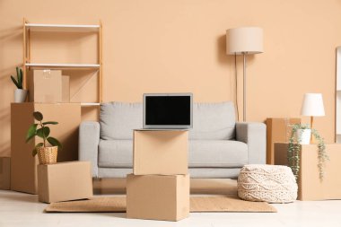 Gri kanepe, dizüstü bilgisayar ve bej duvarın yanında bir sürü paket olan oturma odasının içinde.