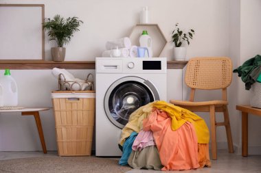 Çamaşır sepetli çamaşır makinesi, kirli çamaşırlar ve deterjanlar çamaşır odasında beyaz duvarın yanında.