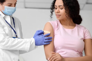 Genç Afro-Amerikalı kadın klinikte aşıdan sonra doktordan yama alıyor.