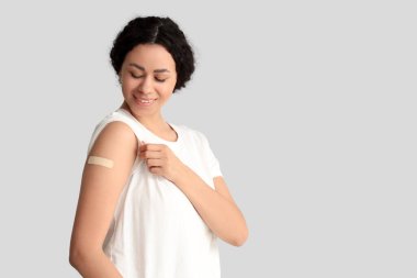 Hafif arkaplandaki aşıdan sonra tıbbi yaması olan genç bir Afro-Amerikalı kadın.