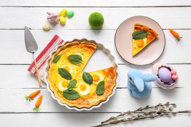 Cut Easter egg tart with toy bunnies and pussy willow branches on white wooden background