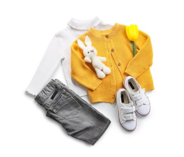 Beyaz arka planda şık çocuk kıyafetleri, tavşan oyuncağı ve lale çiçeği.