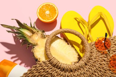 Plaj aksesuarlarıyla dolu çöp torbası ve pembe arka planda olgun meyveler, yakın plan.