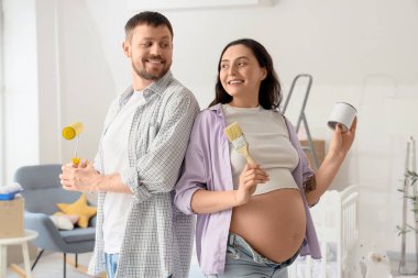 Çocuk odasında boya aletleri olan genç hamile bir çift.