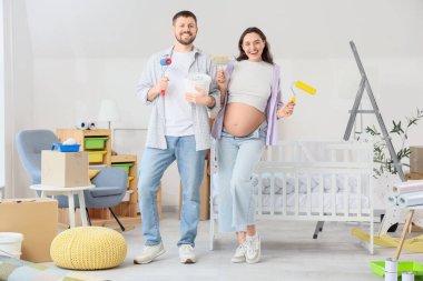Çocuk odasında boya aletleri olan genç hamile bir çift.
