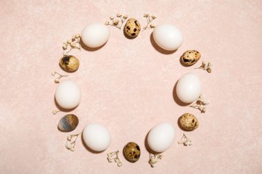 Paskalya yumurtalarından ve pembe arkaplanda çiçeklerden yapılmış çerçeve