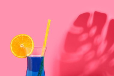 Bir bardak lezzetli kokteyl ve pembe arka planda palmiye yaprağı gölgesi.