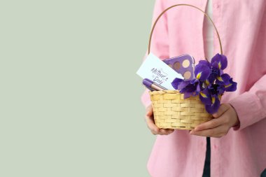 Beyaz arkaplanda anneler günü için çiçek, kartpostal ve kozmetik taşıyan sepet taşıyan genç bir kadın.