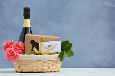 Karanfilli sepet, şampanya şişesi ve Anneler Günü için çikolatalı şekerler mavi grunge arka planda.