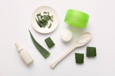 Beyaz arkaplanda kesilmiş aloe vera yaprağı olan farklı kozmetik ürünleri