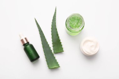 Beyaz arkaplanda aloe vera yaprakları olan farklı kozmetik ürünler