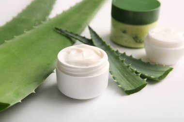 Beyaz arka planda aloe vera yapraklı kozmetik kremi kavanozları.