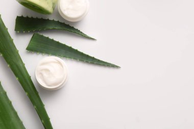 Beyaz arka planda aloe vera yapraklı kozmetik kremi kavanozları.