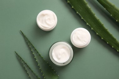 Yeşil arka planda aloe vera yapraklı kozmetik kremi kavanozları.