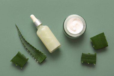 Bir şişe kozmetik yağı ve yeşil arka planda kesilmiş aloe vera yaprağı ile bir kavanoz krema.