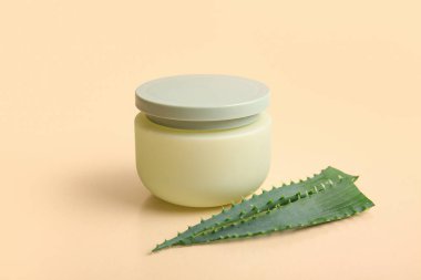 Bej arka planda aloe vera yapraklı bir kavanoz kozmetik kremi.
