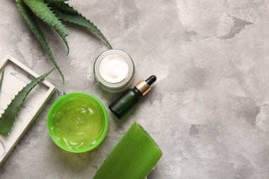 Gri arkaplanda aloe vera yaprakları olan farklı kozmetik ürünler