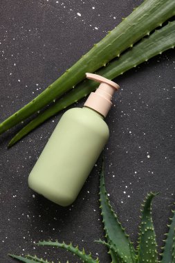Siyah arka planda aloe vera yapraklı bir şişe kozmetik ürünü.