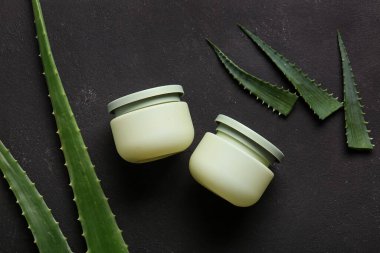 Siyah arka planda aloe vera yapraklı kozmetik kremi kavanozları.