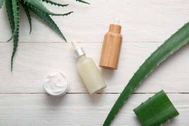Beyaz ahşap arka planda aloe vera yapraklı kozmetik yağı ve krema kavanozu.