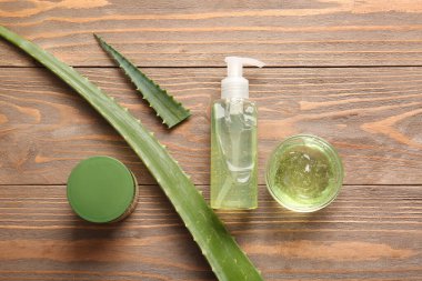 Ahşap zemin üzerinde aloe vera yaprakları olan farklı kozmetik ürünleri