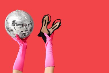 Disko topu ve kırmızı arka planda yüksek topuklu kadın elleri. Balo konsepti