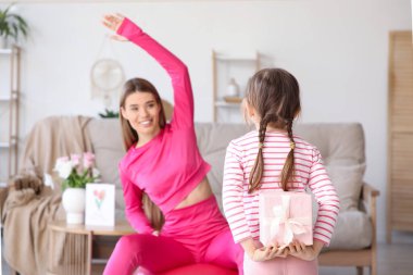 Arkasında hediye kutusu olan sevimli küçük kız evde egzersiz yapan annesine sürpriz yapıyor. Anneler Günü kutlaması