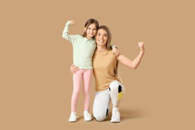 Sportif genç anne ve tatlı küçük kızı bej arka planda kaslarını gösteriyorlar. Anneler Günü kutlaması