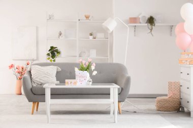 Anneler Günü için dekore edilmiş aydınlık oturma odasının içinde kanepe ve masa var.