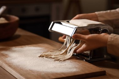 Genç bir kadın karanlık mutfakta makineyle makarna yapıyor, yakın plan.