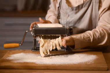 Genç bir kadın karanlık mutfakta makineyle makarna yapıyor, yakın plan.