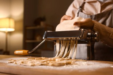 Genç bir kadın karanlık mutfakta makineyle makarna yapıyor, yakın plan.