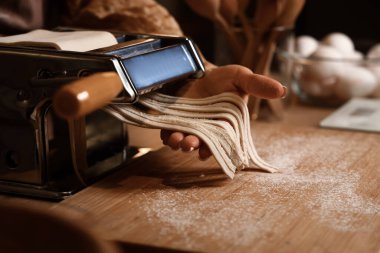 Genç bir kadın karanlık mutfakta makineyle makarna yapıyor, yakın plan.