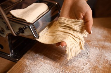 Genç bir kadın karanlık mutfakta makineyle makarna yapıyor, yakın plan.