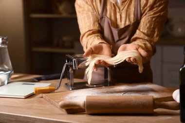 Genç bir kadın karanlık mutfakta makineyle makarna yapıyor.