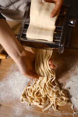 Genç bir kadın karanlık mutfakta makineyle makarna yapıyor.