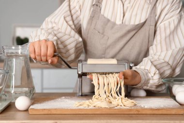 Mutfaktaki masada makineyle makarna yapan genç kadın.