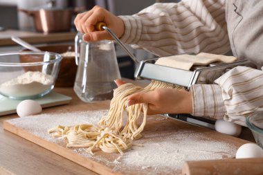 Mutfaktaki masada makineyle makarna yapan genç kadın.