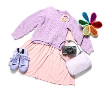 Beyaz arka planda oyuncakları ve kamerası olan küçük bir kız giysisi.